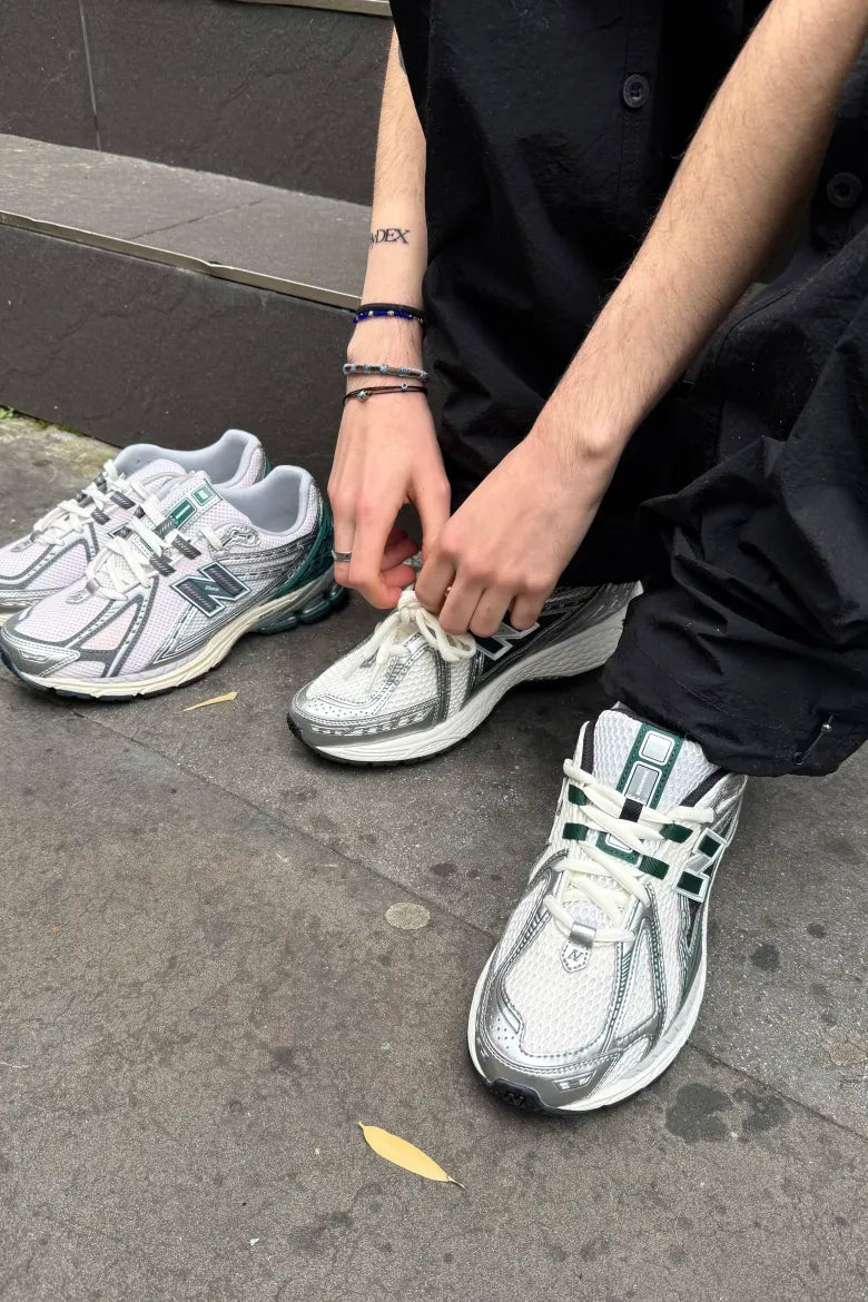 Man lacing up a pair of New Balance M1906R sneakers in white and metallic silver, part of an END. editorial on ways to style the sneaker.