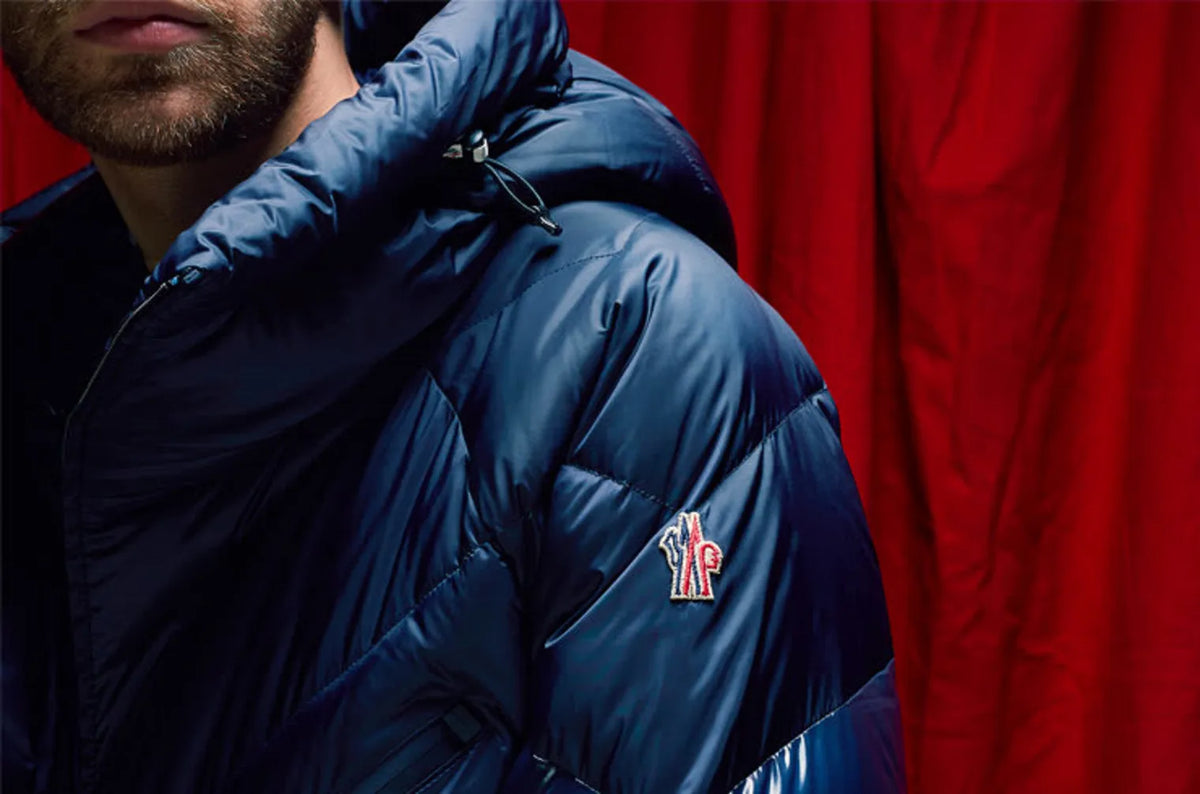 Zoomed‑in view of a man wearing a navy Moncler puffer coat, showing the shoulder logo badge.