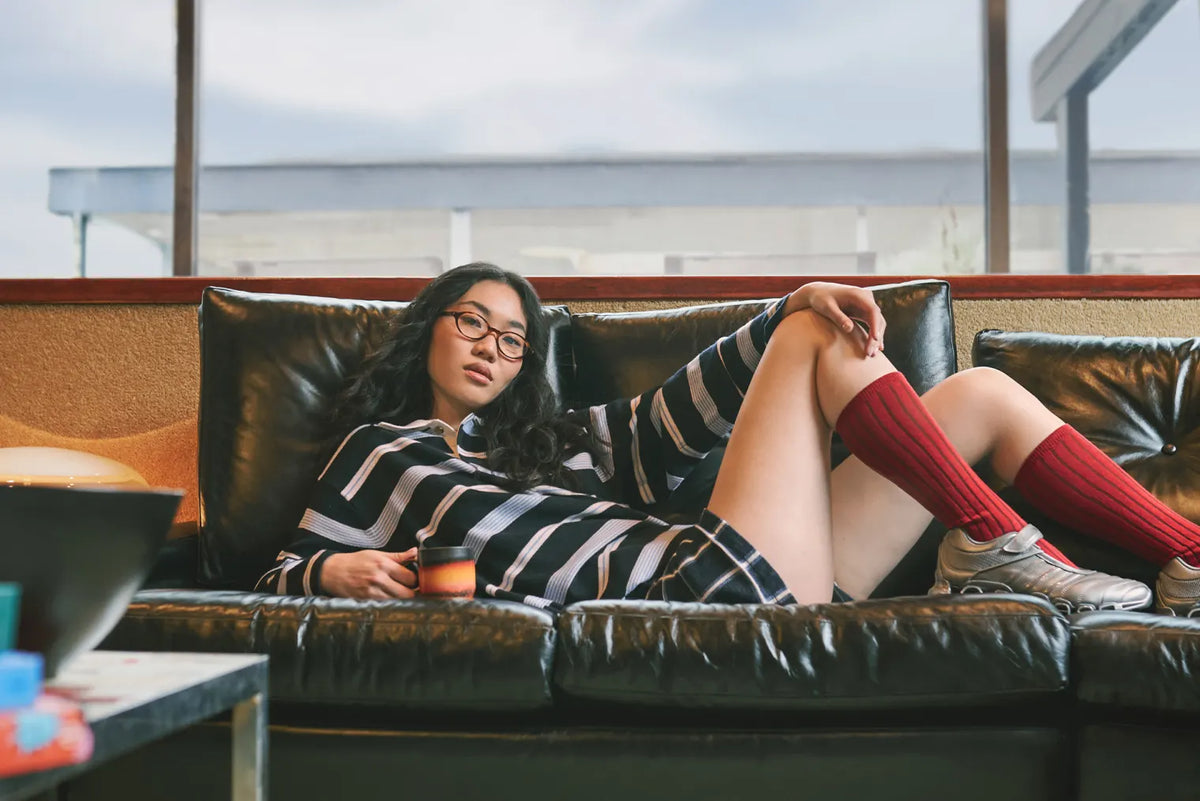 Woman wearing a GUEST IN RESIDENCE rugby polo and plaid shorts, Saint Laurent glasses, and adidas x Taqwa Bint Ali Megaride sneakers, styled in the END. Spring 2025 Editorial.