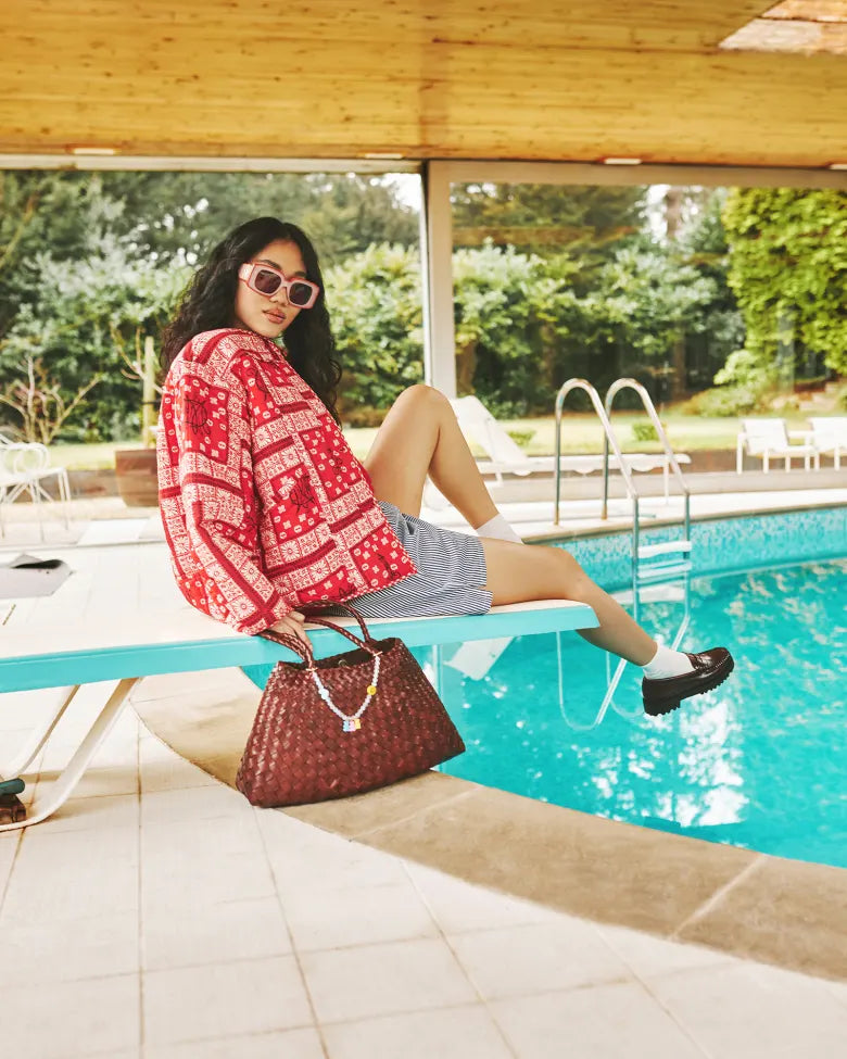 END. Spring 25 Editorial model wearing a Damson Madder jacket, styled with DONNI stripe shorts, Bass Weejuns loafers, sunglasses, and a Dragon Diffusion bag.