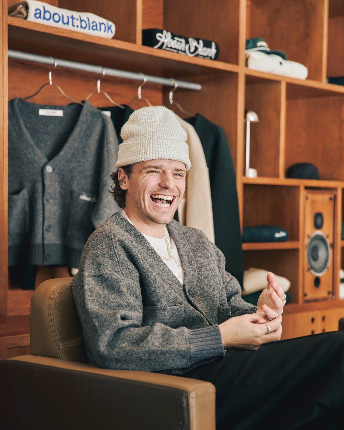 A man in a beanie sitting on a chair and smiling.