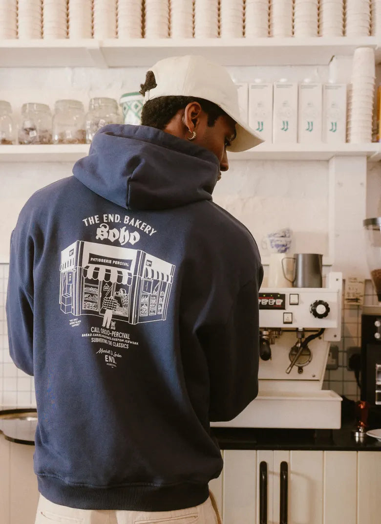 Man in bakery wearing a Percival hat and hoodie