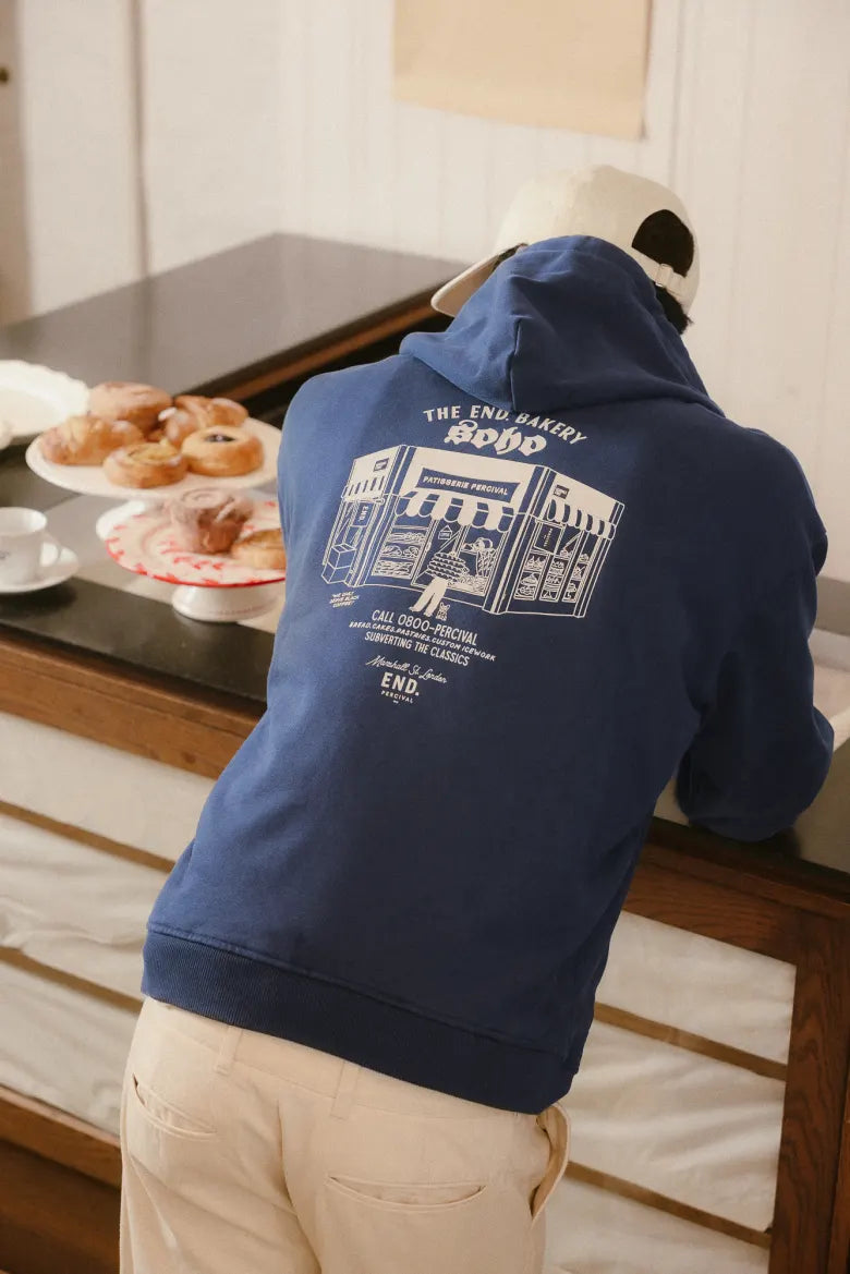 Man in bakery wearing a Percival hat and hoodie