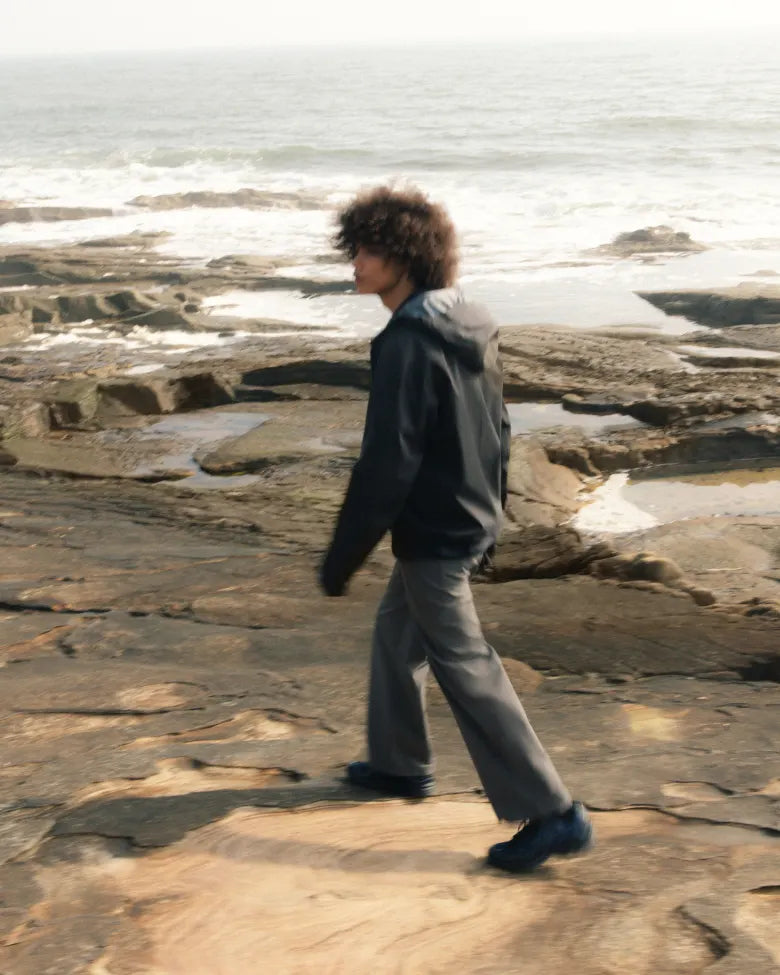 A man wearing the END. x Mizuno Wave Rider 10 sneaker with the sea in the background.