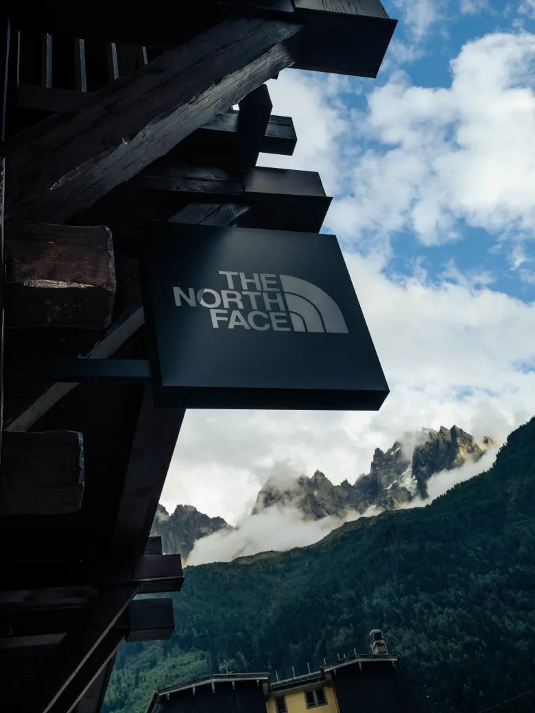 A The North Face shop sign with mountains and a cloudy blue sky in the background.