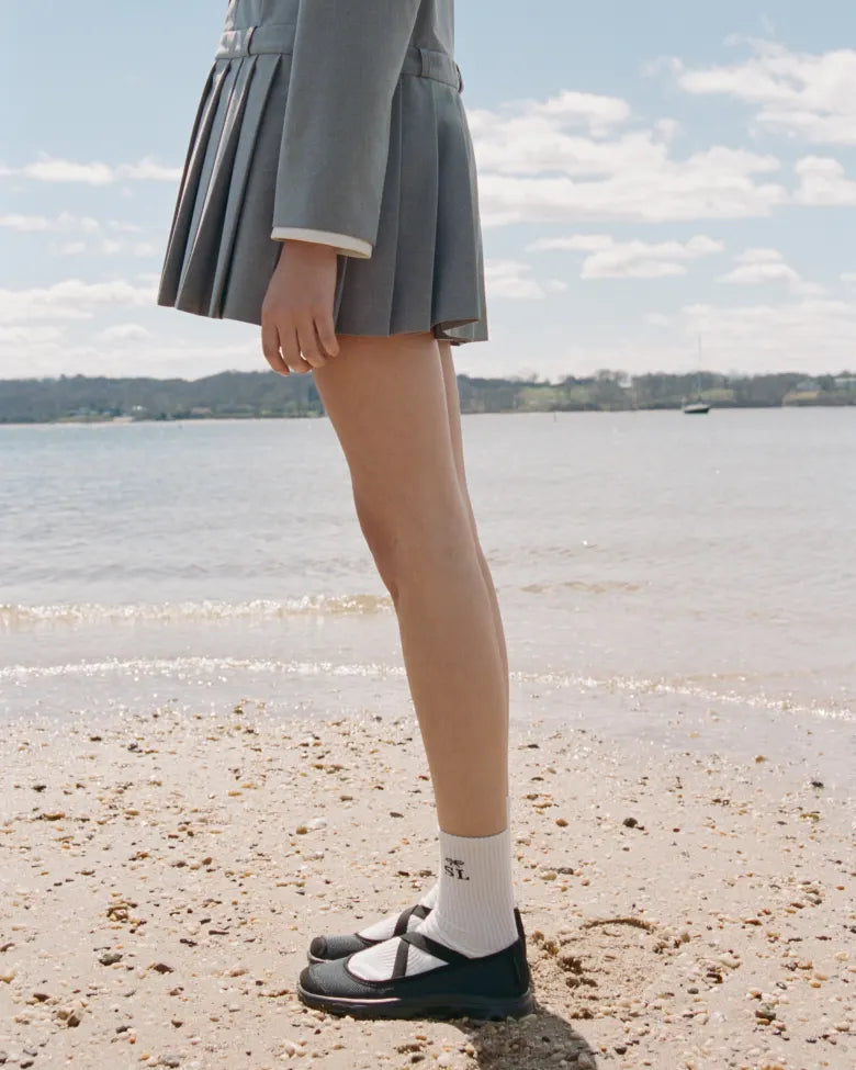 A lady in a skirt wearing the Salomon x Sandy Liang collaboration footwear on a beach.