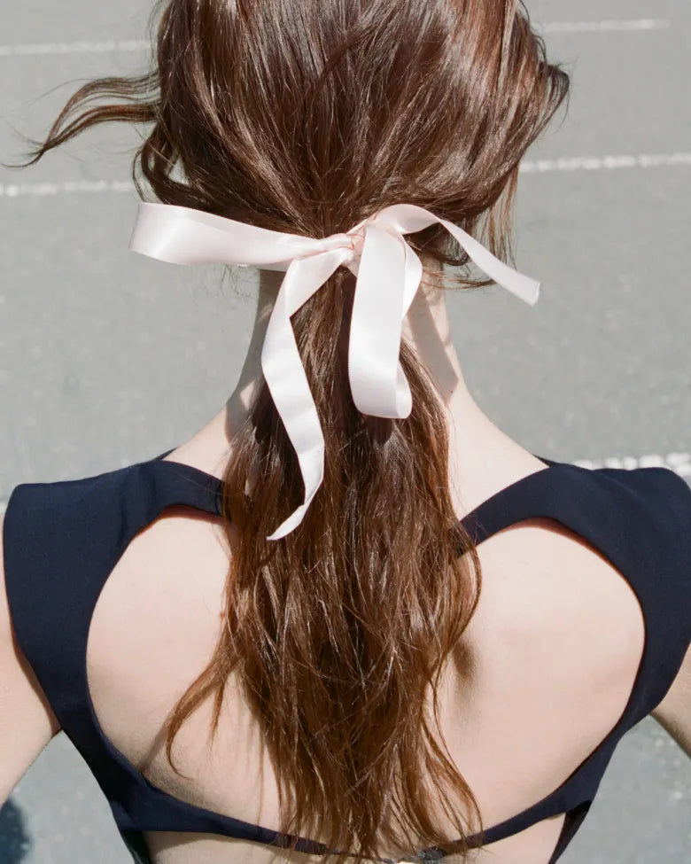 A lady with a pink ribbon in her long brown hair.