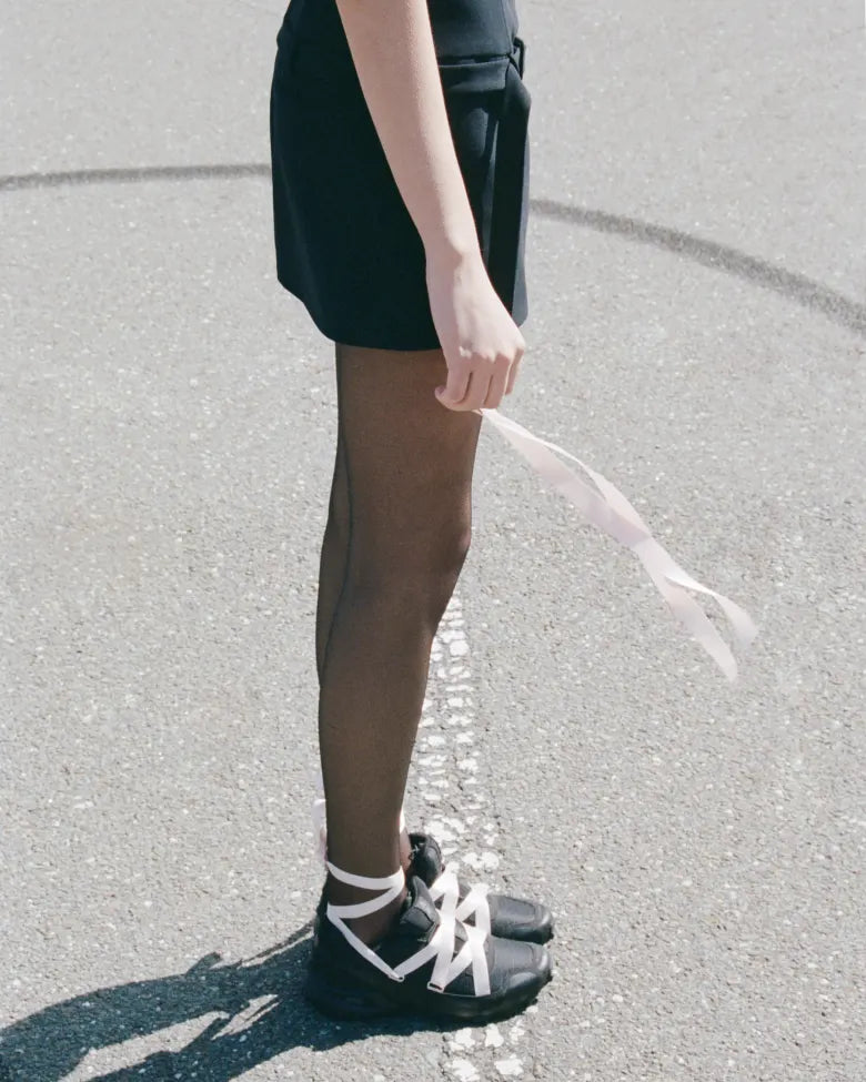 A lady wearing the Salomon x Sandy Liang collaboration footwear holding a ribbon.